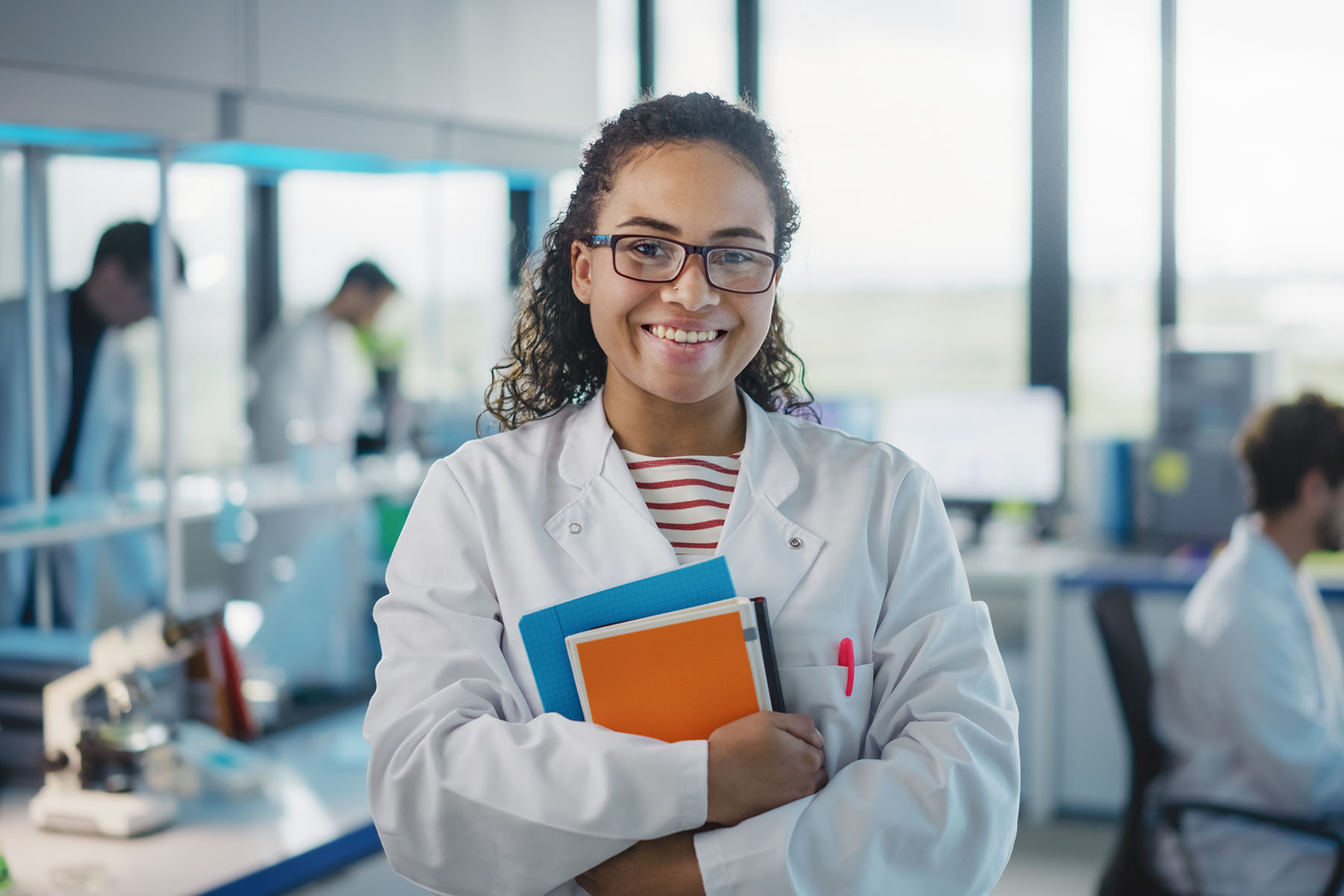 Woman in a lab wearing a lab coat and holding books