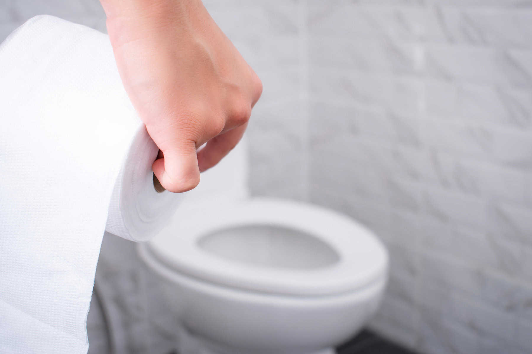 A hand holding toilet paper with a toilet in the background